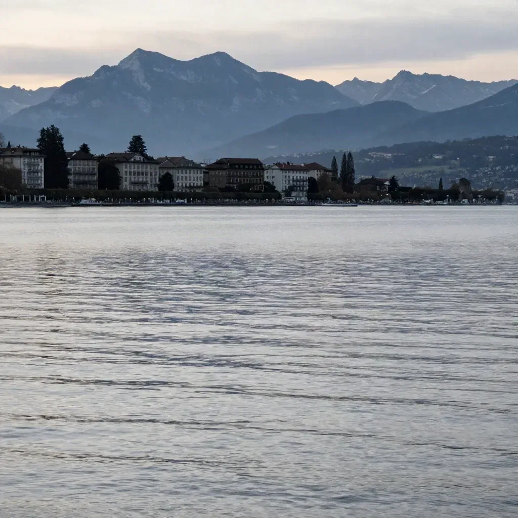 Le Léman au soir, rive de Genève et Alpes lointaines dans une brume douce.